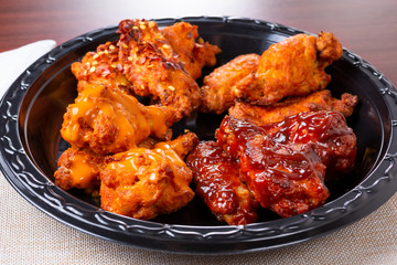 A view of a plate of chicken wings with several varieties of sauces and rubs, in a restaurant or kitchen setting.