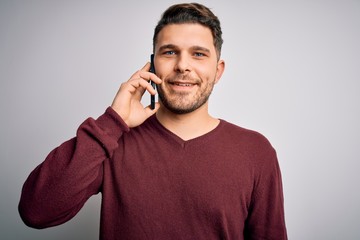 Young man with blue eyes speaking on the phone having a conversation on smartphone with a happy face standing and smiling with a confident smile showing teeth
