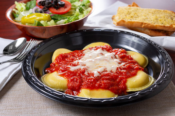 A view of a ravioli dinner, with a side salad and garlic bread, in a restaurant or kitchen setting.