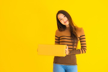 Beautiful young asian woman holding cardboard box in her hand on yellow background