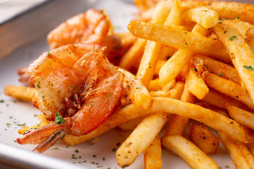 A closeup view of a tray of cajun style french fries with some fried shrimp, in a restaurant or kitchen setting.