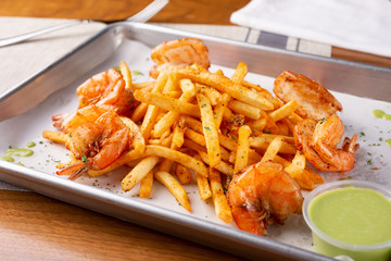 A view of an appetizer tray of cajun style french fries with fried shrimp, in a restaurant or kitchen setting.