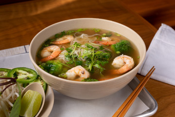 A view of a pho soup bowl with shrimp and vegetables, in a restaurant or kitchen setting.