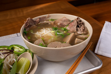 A view of a pho soup bowl with several varieties of meat, in a restaurant or kitchen setting.