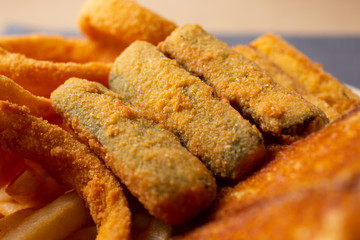 A closeup view of zucchini sticks among several other deep fried appetizers, in a restaurant or kitchen setting.