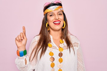 Young hispanic hippie woman wearing fashion boho style and sunglasses over pink background pointing finger up with successful idea. Exited and happy. Number one.