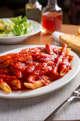 A view of a penne pasta Italian dinner, with a side salad and garlic bread, in a restaurant or kitchen setting.