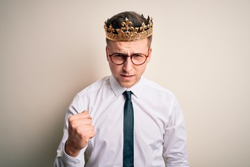 Young handsome caucasian business man wearing golden crown over isolated background angry and mad raising fist frustrated and furious while shouting with anger. Rage and aggressive concept.