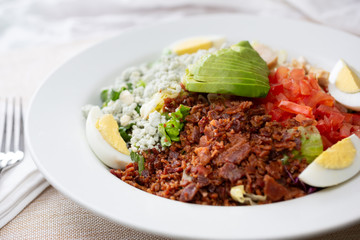 A closeup view of a bowl of cobb salad, in a restaurant or kitchen setting.