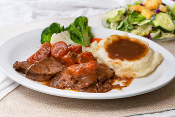 A view of a plate of pot roast dinner, with a side salad, in a restaurant or kitchen setting.