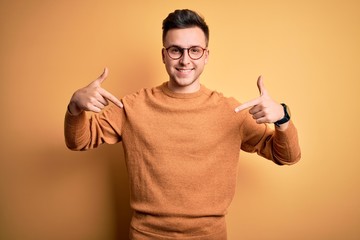 Young handsome caucasian man wearing glasses and casual winter sweater over yellow background...