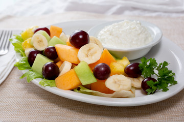 A view of a fruit salad entree with a side of cottage cheese, in a restaurant or kitchen setting.