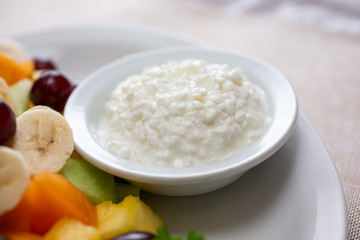 A closeup view of a small bowl of cottage cheese, part of a fruit salad plate.