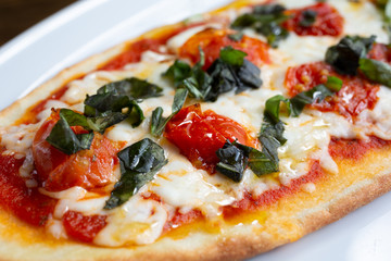 A view of a plate of margherita style flatbread pizza, in a restaurant or kitchen setting.