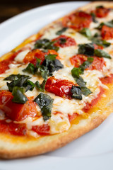A view of a plate of margherita style flatbread pizza, in a restaurant or kitchen setting.