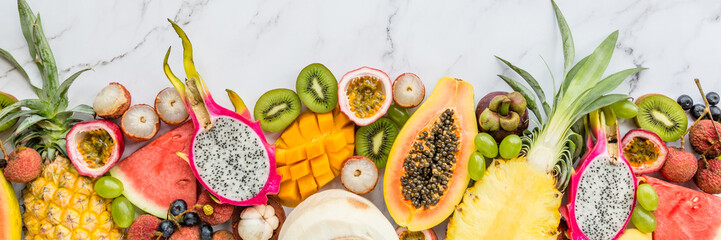 Fresh exotic fruits and tropical palm leaves on white marble background - papaya, mango, pineapple, passion fruit, dragon fruit, melon. Healthy food and diet concept