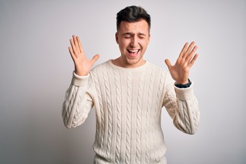 Fototapeta premium Young handsome caucasian man wearing casual winter sweater over white isolated background celebrating mad and crazy for success with arms raised and closed eyes screaming excited. Winner concept