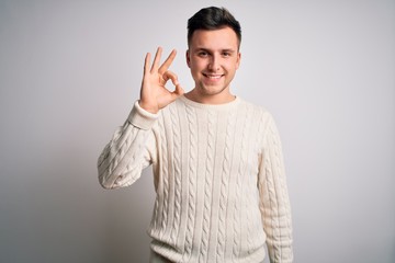 Young handsome caucasian man wearing casual winter sweater over white isolated background smiling positive doing ok sign with hand and fingers. Successful expression.