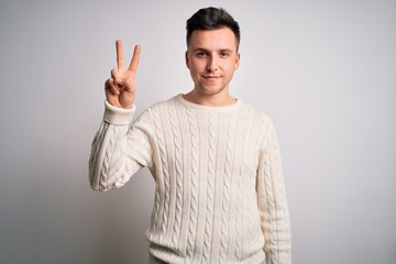 Naklejka premium Young handsome caucasian man wearing casual winter sweater over white isolated background showing and pointing up with fingers number two while smiling confident and happy.
