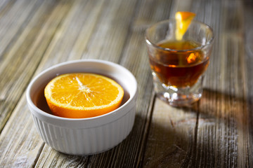 A view of a shot of whiskey and a half orange inside a ramekin bowl.