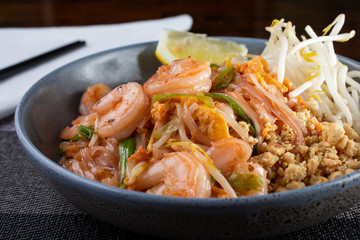 A closeup side view of a bowl of shrimp pad Thai, in a restaurant or kitchen setting.
