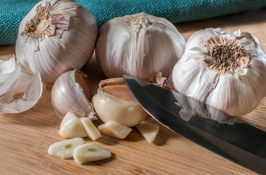 Macro photography or close up image of a group of garlic and garlic slices on a wooden cutting board and a knife on the side