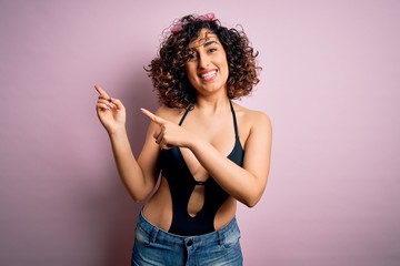 Young beautiful arab woman on vacation wearing swimsuit and sunglasses over pink background smiling and looking at the camera pointing with two hands and fingers to the side.