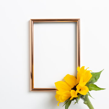 Empty photo frame with yellow sunflower on white background. top view, copy space