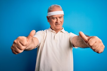 Middle age hoary sportsman doing sport wearing sportswear over isolated blue background approving doing positive gesture with hand, thumbs up smiling and happy for success. Winner gesture.