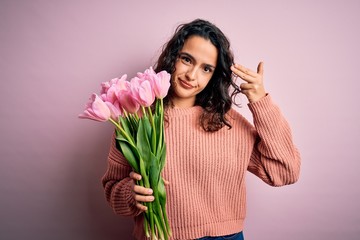 Young beautiful romantic woman with curly hair holding bouquet of pink tulips Shooting and killing oneself pointing hand and fingers to head like gun, suicide gesture.