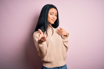 Young beautiful chinese woman wearing casual sweater over isolated pink background pointing fingers to camera with happy and funny face. Good energy and vibes.