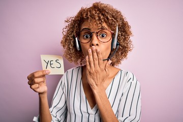 African american call center agent woman using headset holding reminder with yes message cover...