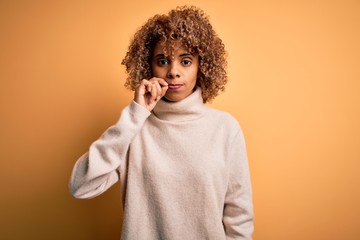 Young beautiful african american woman wearing turtleneck sweater over yellow background mouth and lips shut as zip with fingers. Secret and silent, taboo talking