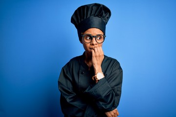 Young african american chef woman wearing cooker uniform and hat over blue background looking stressed and nervous with hands on mouth biting nails. Anxiety problem.