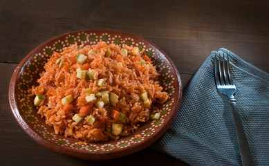 Mexican food, Mexican rice with vegetables and tomato puree on a mug plate or clay plate, with a blue napkin and a fork on the side