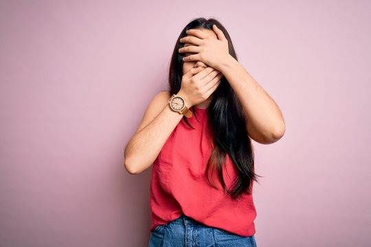 Young brunette woman wearing casual summer shirt over pink isolated background Covering eyes and mouth with hands, surprised and shocked. Hiding emotion