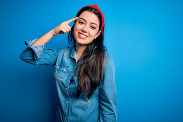 Young brunette woman wearing casual denim shirt over blue isolated background Smiling pointing to head with one finger, great idea or thought, good memory