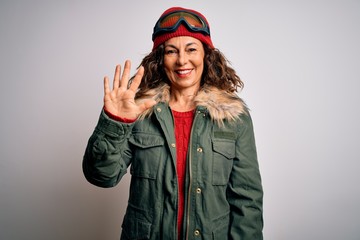 Middle age skier woman wearing snow sportswear and ski goggles over white background showing and pointing up with fingers number five while smiling confident and happy.