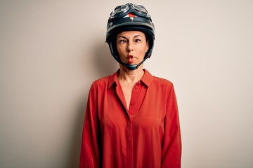 Middle age motorcyclist woman wearing motorcycle helmet over isolated white background making fish face with lips, crazy and comical gesture. Funny expression.