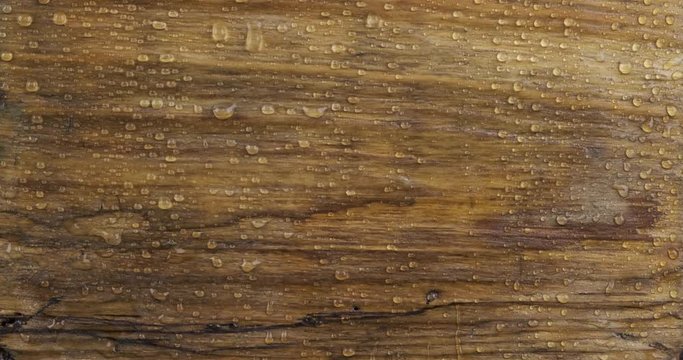 Drops of rain fall on an old wooden board and flow down streams down. Close-up.