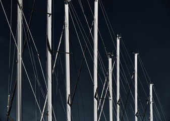 The number of masts of sailboats with the blue sky on a background, a sail regatta, reflection of masts on water, ropes and aluminum, Bright colors