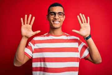 Naklejka premium Young handsome african american man wearing casual striped t-shirt and glasses showing and pointing up with fingers number ten while smiling confident and happy.