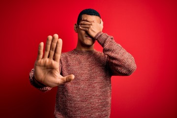 Naklejka premium Young handsome african american man wearing casual sweater standing over red background covering eyes with hands and doing stop gesture with sad and fear expression. Embarrassed and negative concept.