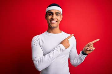 Young handsome african american sportsman wearing sportswear over red background smiling and looking at the camera pointing with two hands and fingers to the side.