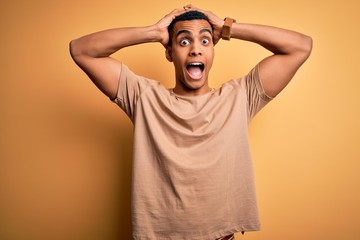 Fototapeta na wymiar Young handsome african american man wearing casual t-shirt standing over yellow background Crazy and scared with hands on head, afraid and surprised of shock with open mouth