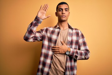 Young handsome african american man wearing casual shirt standing over yellow background Swearing...