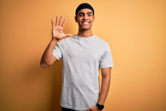 Handsome african american sportsman doing sport wearing sportswear over yellow background showing and pointing up with fingers number five while smiling confident and happy.