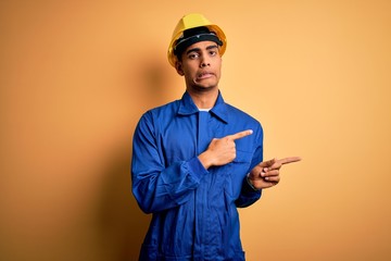 Young handsome african american worker man wearing blue uniform and security helmet Pointing aside worried and nervous with both hands, concerned and surprised expression