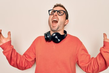 Obraz premium Young handsome man listening to music using headphones over isolated white background crazy and mad shouting and yelling with aggressive expression and arms raised. Frustration concept.