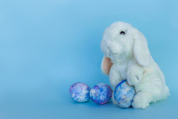 Easter white toy rabbit with colorful space-colored eggs on a blue background. Happy Easter card with copy space for text.